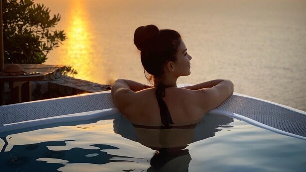 Eine Person entspannt sich am Pool mit Blick auf den Sonnenuntergang.
