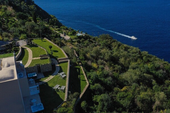 An aerial view of a coastal property with a landscaped garden, a swimming pool, and a view of the sea.