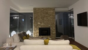 Ein modernes Wohnzimmer mit einem weißen Sofa, einem Kamin aus Stein und einer Deckenleuchte.