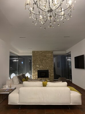 Una sala de estar moderna con un sofá blanco, una chimenea de piedra y una araña.