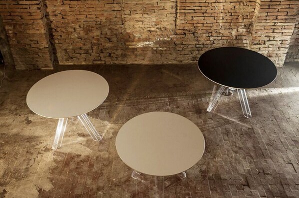 Tres mesas redondas con patas transparentes en una habitación con pared de ladrillo.