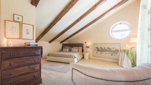 Une chambre confortable située dans les combles, avec une commode en bois, un lit avec des oreillers, une table de chevet et une œuvre d’art encadrée accrochée au mur.