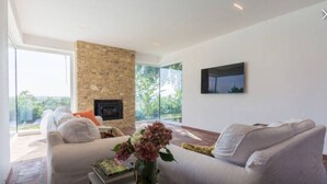 Un salon moderne doté d’une cheminée en pierre, de sièges confortables et d’une grande fenêtre offrant une vue sur l’extérieur.