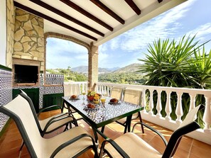 A patio with a table set for two, a stone oven, and a view of mountains.