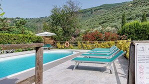 A pool area with lounge chairs and a lifebuoy, surrounded by greenery and hills.