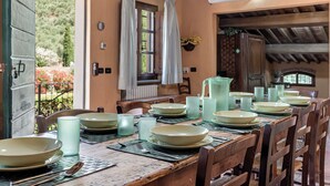 A dining table set with plates, glasses, and cutlery, with a view of a garden through an open door.