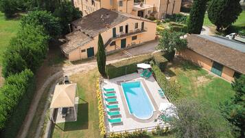 An aerial view of a residential property with a swimming pool, multiple buildings, and surrounding greenery.