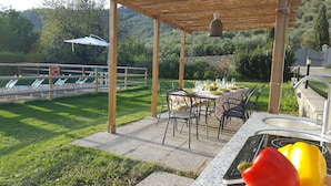 An outdoor patio with a table set for dining, surrounded by chairs, and a grill area with a sink.