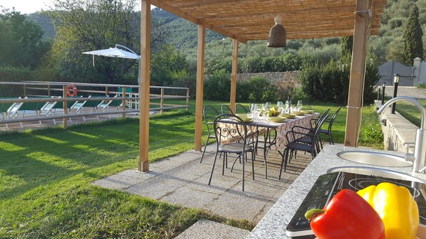 Une terrasse extérieure avec une table dressée pour les repas, entourée de chaises, et un espace barbecue équipé d’un évier.