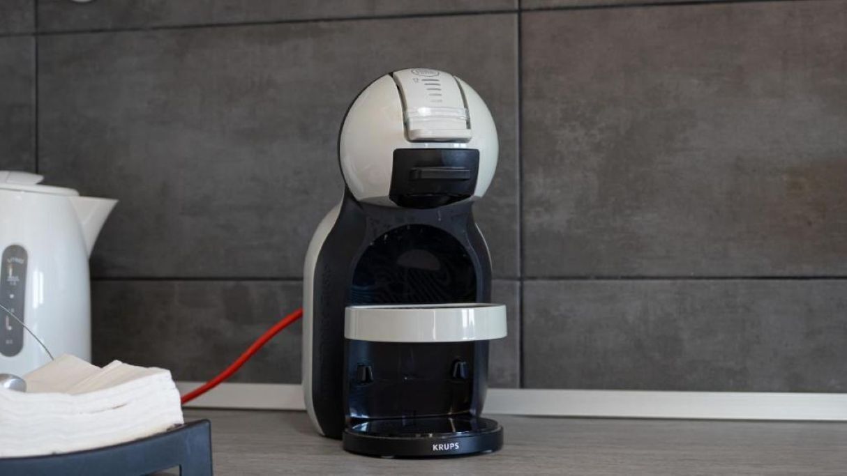 Une machine à café de la marque Krups, une bouilloire blanche et un fil rouge sur un sol carrelé.