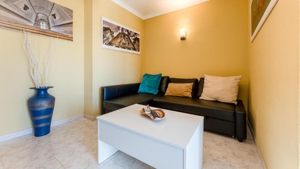 A living room with a sofa, a coffee table, a vase, and a painting on the wall.