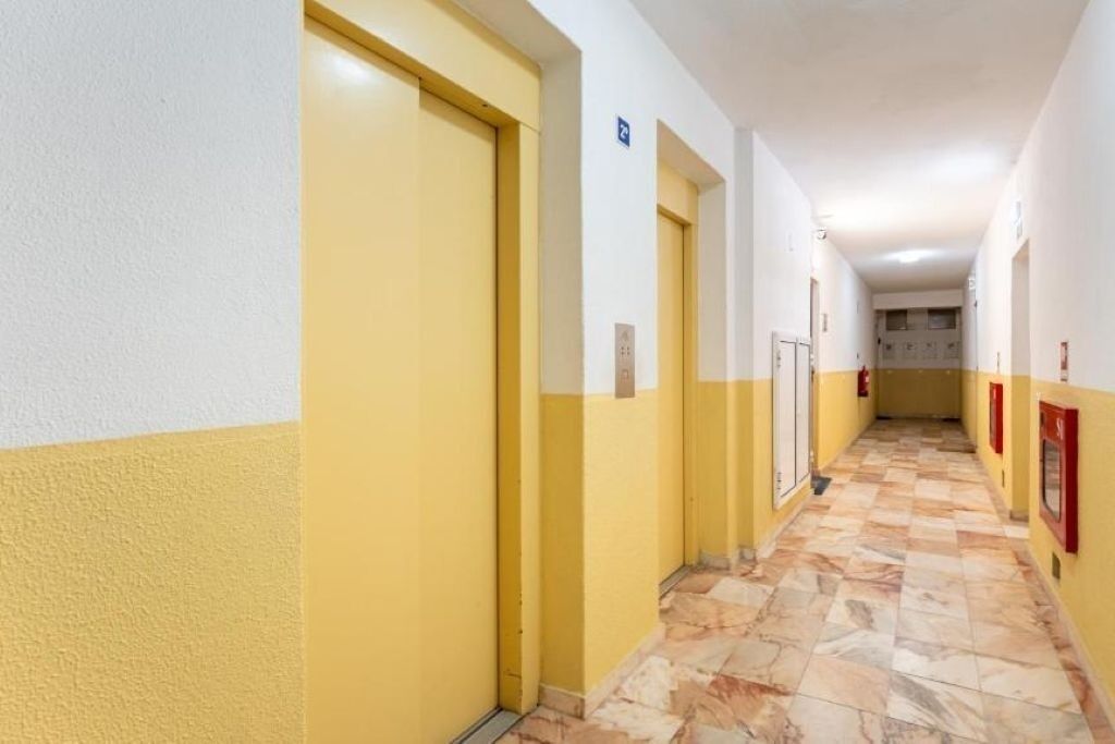 Un couloir aux portes jaunes et aux murs blancs, qui mène à une pièce dont le sol est recouvert de carreaux.