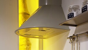 A kitchen with a stainless steel range hood, a gas stove, and a coffee maker. There are two jars on a shelf above the stove.