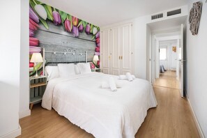 A bedroom with a bed, white bedding, a headboard with a floral mural, a nightstand with a lamp, and a wardrobe. - Boquerón Apartment - In The Station (Málaga)