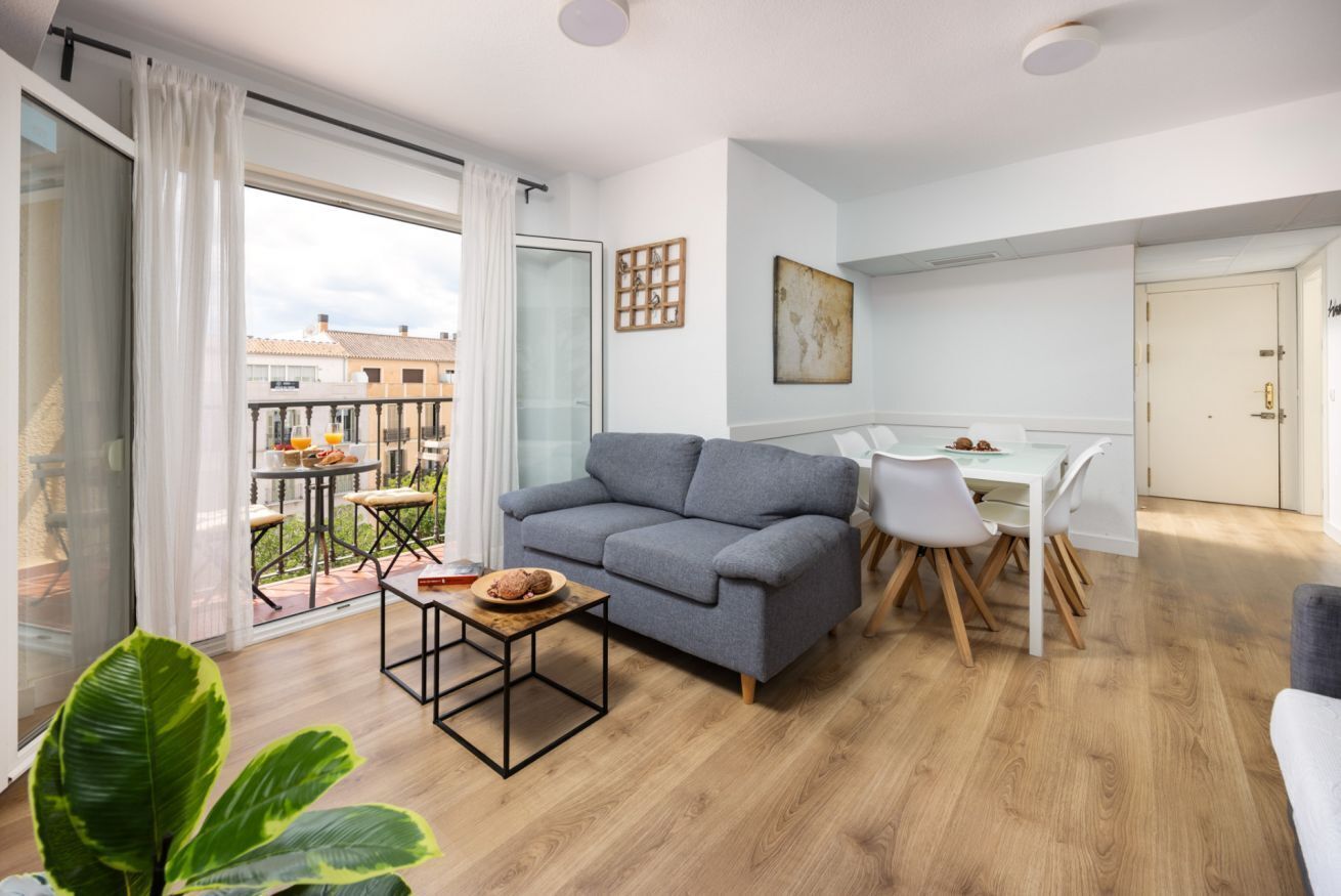 Een modern appartement met een grijze bank, een eettafel met stoelen en een balkon met een tafel en stoelen.