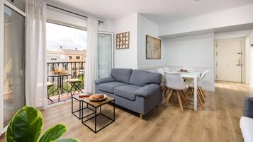 Een modern appartement met een grijze bank, een eettafel met stoelen en een balkon met een tafel en stoelen.