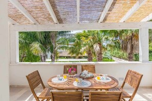Una mesa redonda de madera con cuatro sillas, una ventana que ofrece vista a palmeras y un techo de paja.