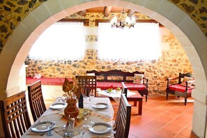 A dining area with stone walls, wooden furniture, and a chandelier. - Stone Villa Olga shared pool & seaview, 3bedrooms, BBQ (Astratigos)
