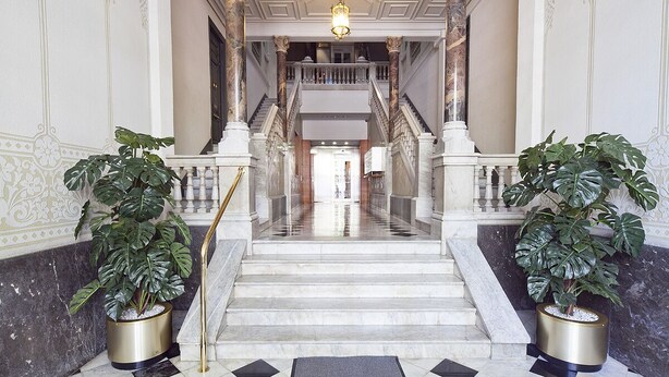 A grand staircase with marble steps and columns, leading to a balcony with a railing.