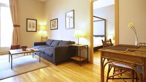 A hotel room with a sofa, a small table, a dining table with chairs, a mirror, and two lamps.