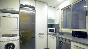 A compact kitchen with a stainless steel refrigerator, a microwave, a dishwasher, and a washing machine.