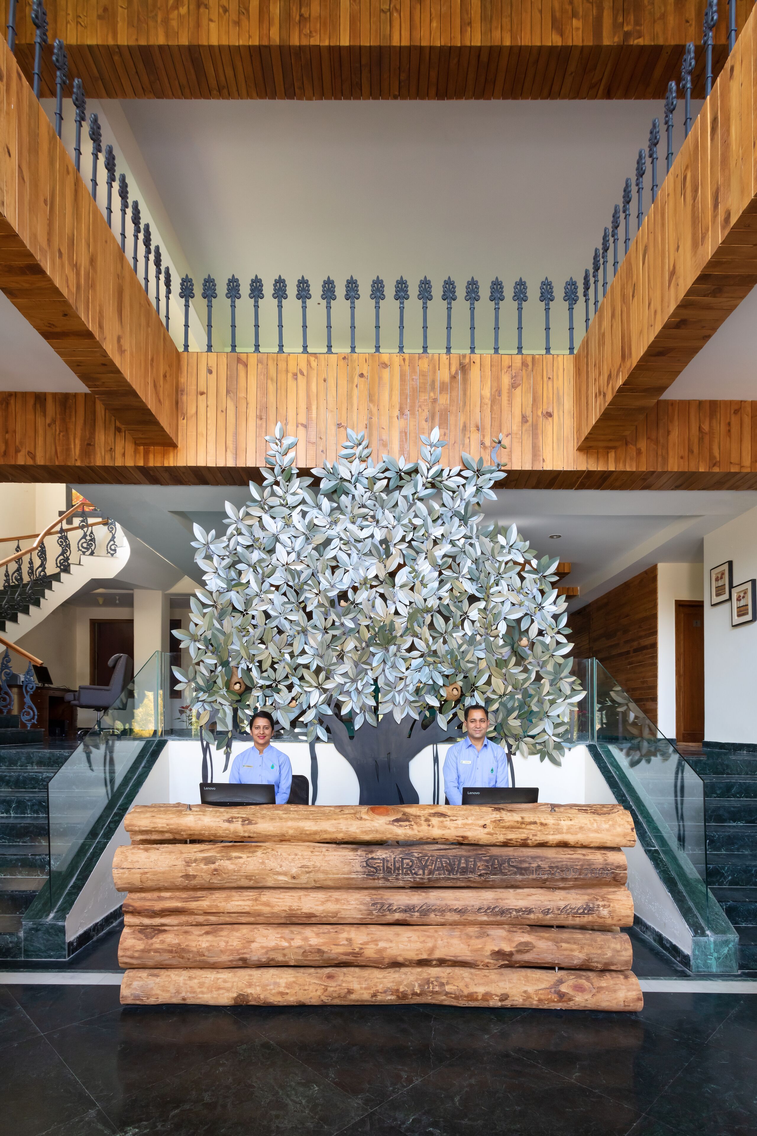 A reception desk with a large artificial tree and two staff members.