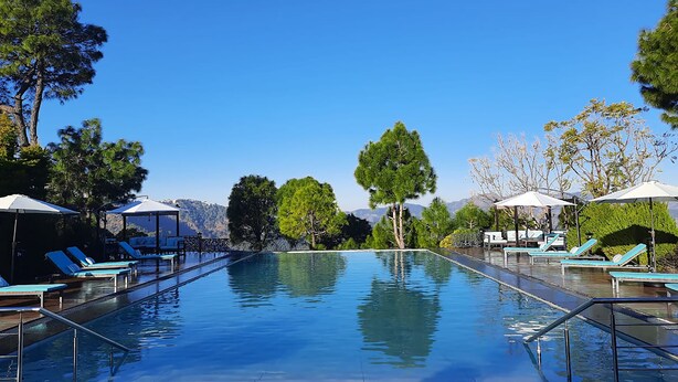 Un cielo azul despejado, una piscina con sillas de descanso y árboles al fondo.