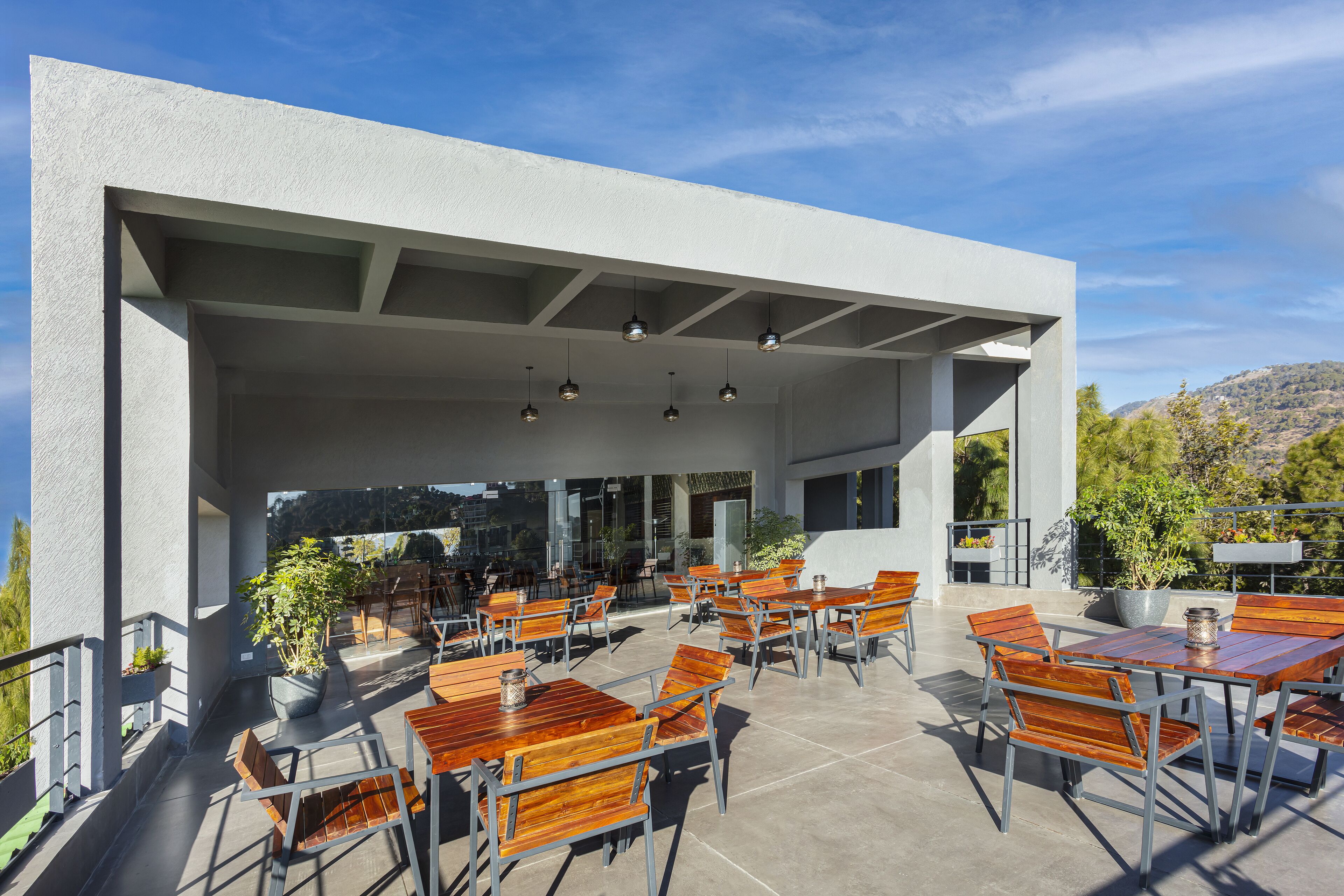 An outdoor patio with wooden tables and chairs, a white building structure, and hanging lights.