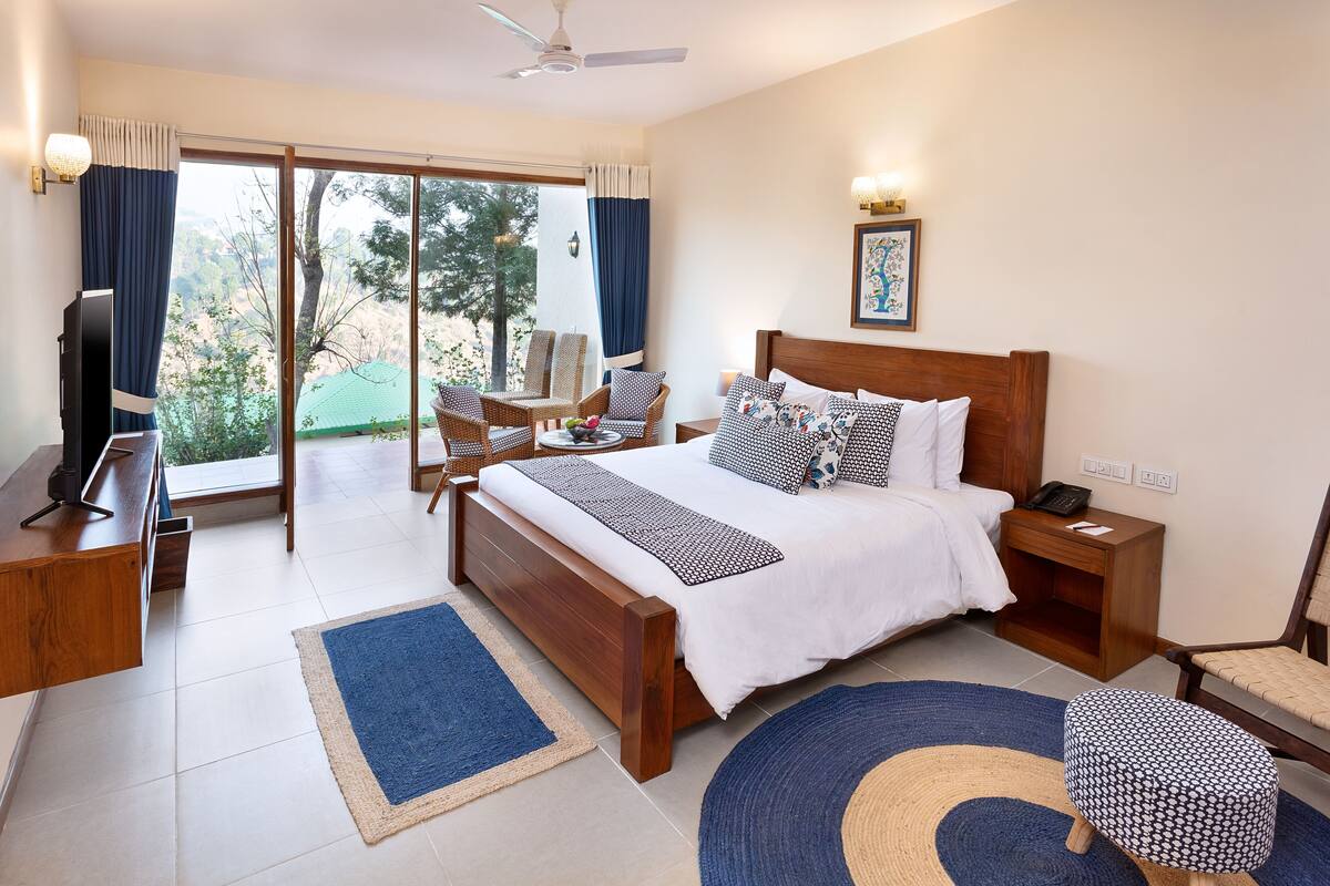A modern hotel room with a large bed, a desk, a chair, and a TV.