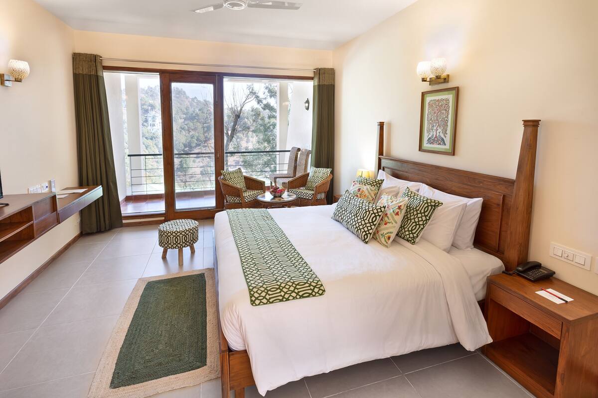 A hotel room with a large bed, a balcony with wicker chairs, and a view of the mountains.