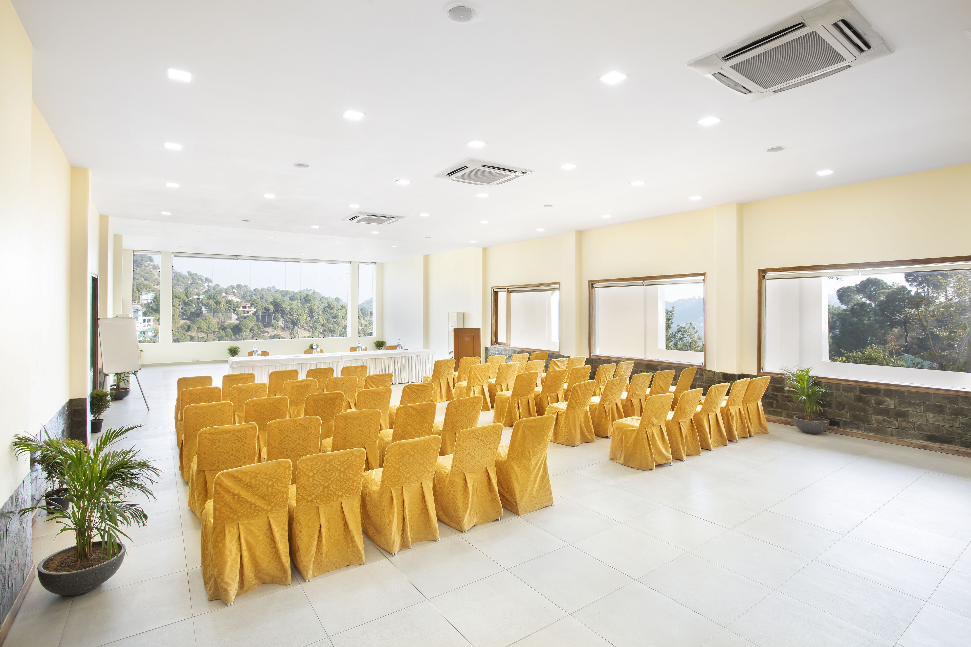 A conference room with rows of chairs, a podium, and large windows with a view of greenery.