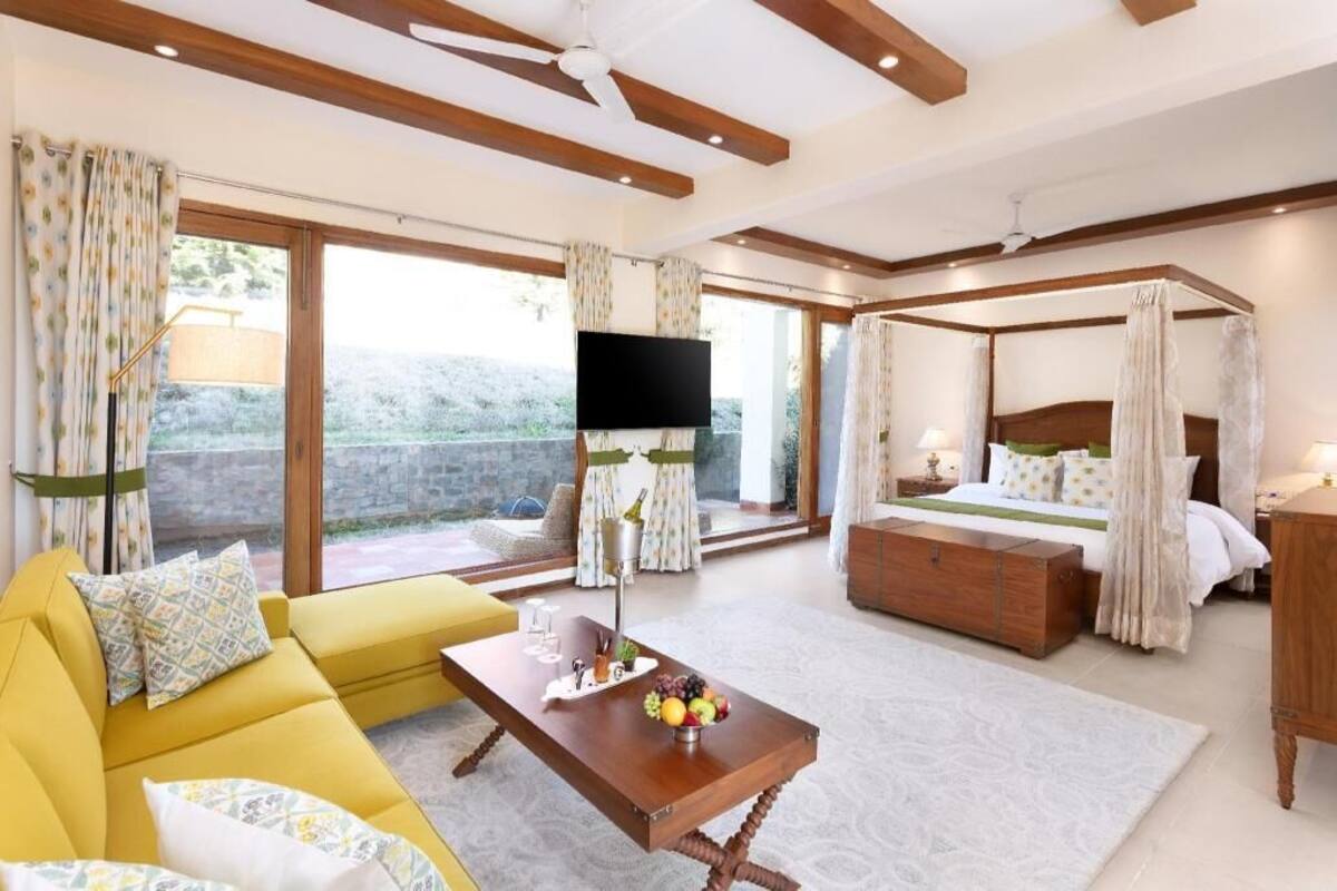 A bedroom with a four-poster bed, a sofa, a TV, and a balcony view.
