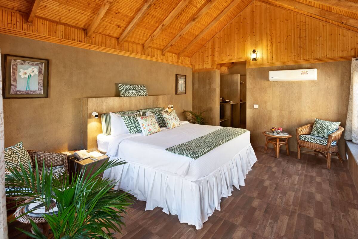 A bedroom with a large bed, two wicker chairs, a small table, and a wall-mounted air conditioner.