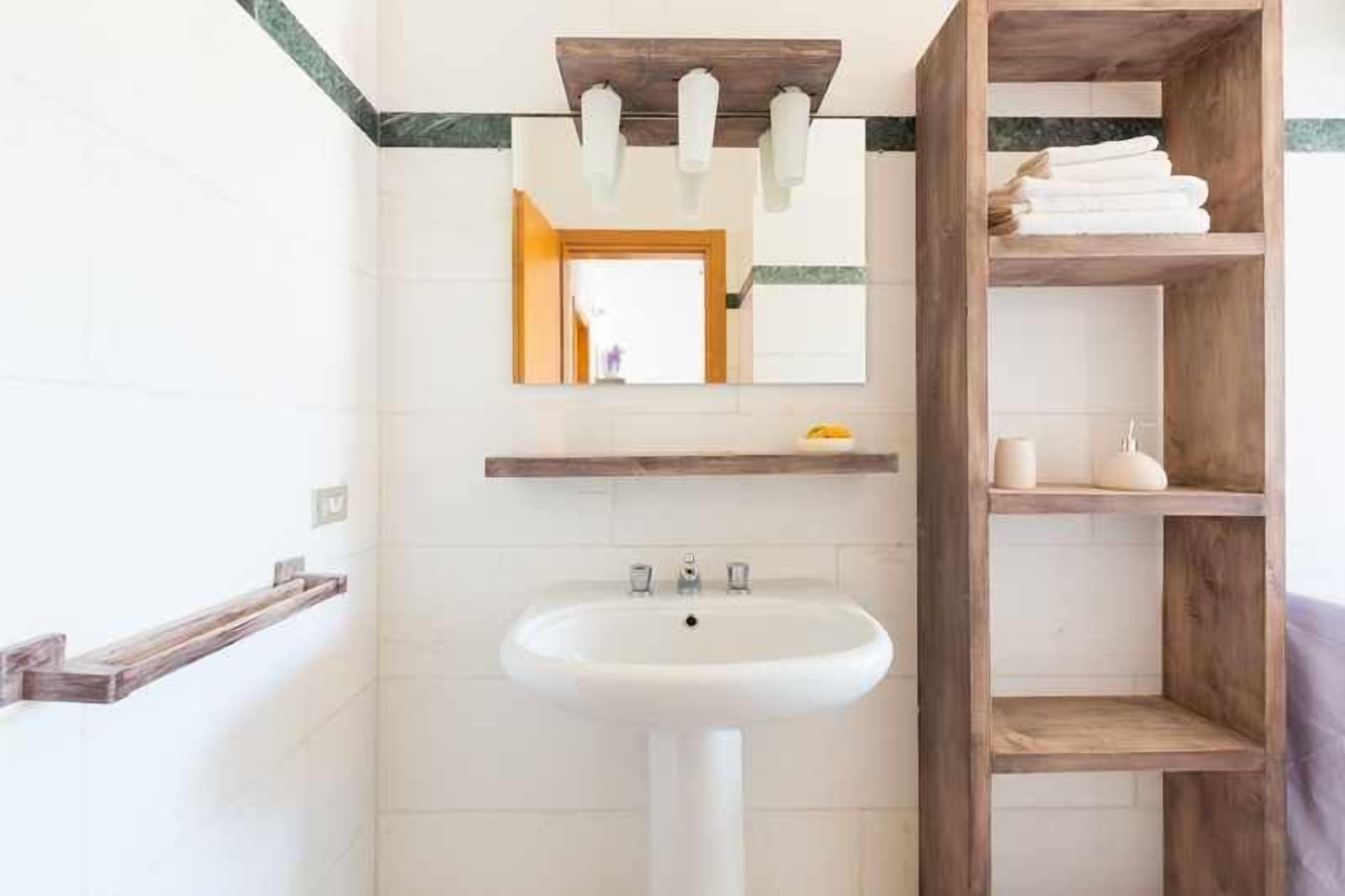 A bathroom with a white sink, wooden shelves, and a mirror.