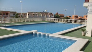 A rectangular swimming pool with clear blue water, surrounded by a white fence and a green lawn. - Apartment in private urbanization with pool and garden area in Santa Pola (Santa Pola)