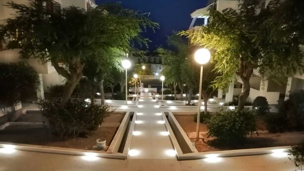 A nighttime view of a courtyard with a central pathway, surrounded by trees and illuminated by street lamps. - Apartment in private urbanization with pool and garden area in Santa Pola (Santa Pola)