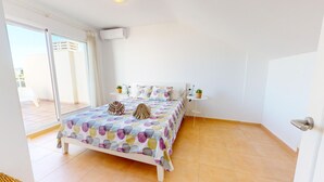 A bedroom with a bed, a small bedside table, a potted plant, and a sliding glass door leading to a balcony. - Maravilloso Ático a tan solo 150 m de la playa. Wifi. A/A. 5 pers. (Dénia)