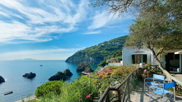 A coastal view with a house overlooking the sea, featuring a balcony with chairs and a table. - Cottage by the Sea in Cartaromana Bay, with a View of Aragonses Castle  (Ischia)