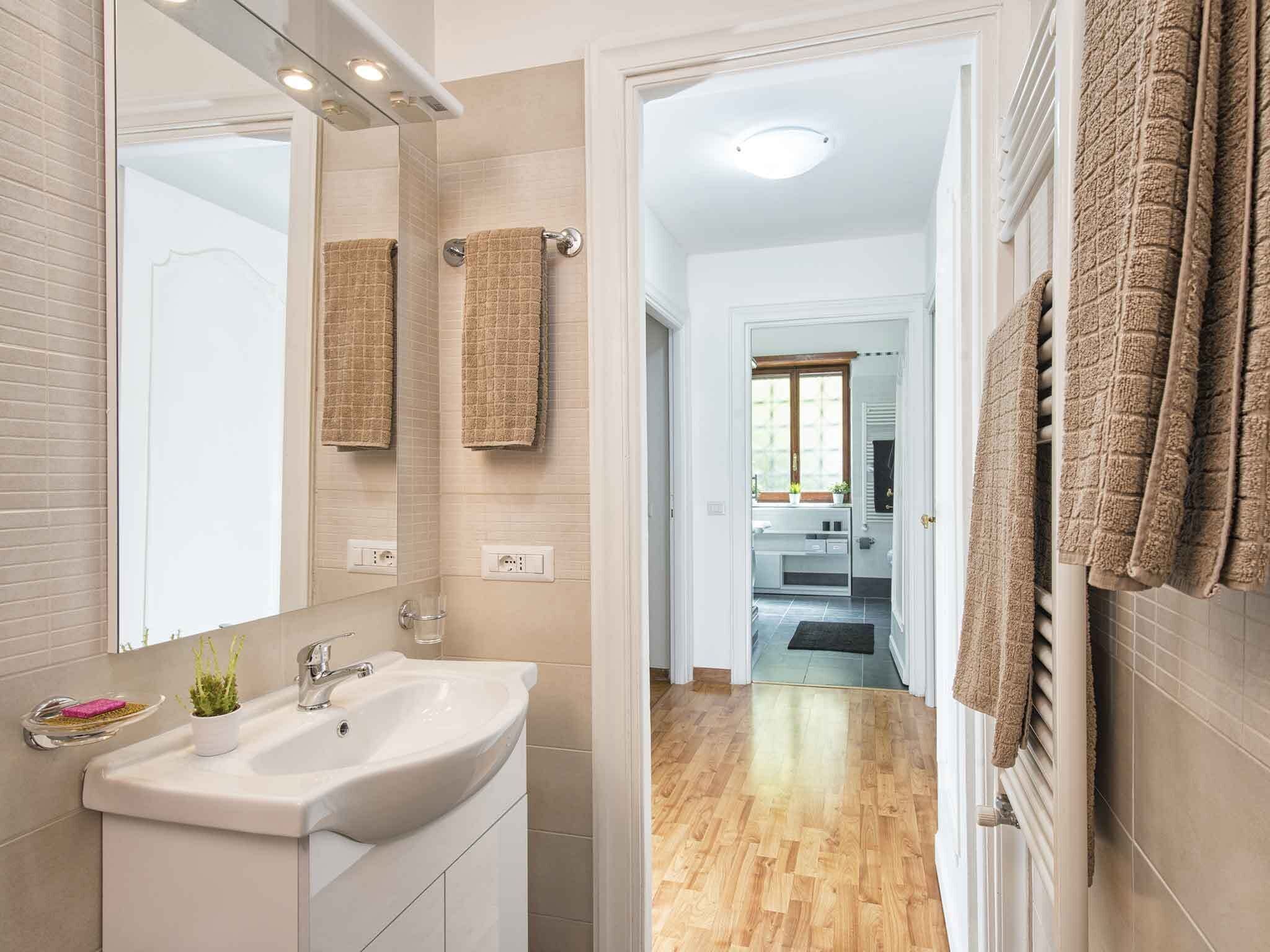 A modern bathroom with a large mirror, a white sink, and a wooden floor leading to a bedroom.