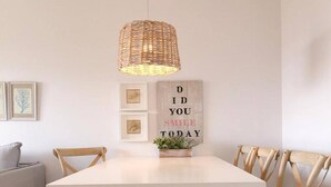 A dining table with a woven light fixture above it, surrounded by wooden chairs.
