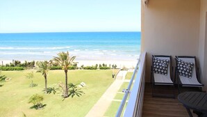 A balcony with a view of the beach, two lounge chairs, and a small table.