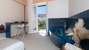 A modern bathroom with a glass bathtub, a white sink, and a small seating area with a chair and table. - Casa Pina Ocean (Sorrento)