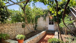 Ein Garten mit Steinsäulen, Kübelpflanzen und einem roten Weg.