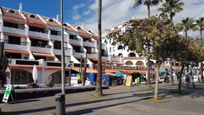 Un edificio de varios pisos con balcones, un restaurante llamado Restaurante Grill El Cedro y palmeras.