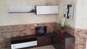 Una sala de estar con un televisor de pantalla plana, un mueble de madera para entretenimiento, una planta en maceta y un estante de pared con adornos.