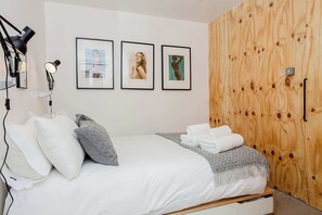 Ein Schlafzimmer mit einem Bett, Kissen, einer Decke, einem Holzschrank und gerahmten Bildern an der Wand.