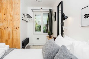 A bedroom with a bed, a radiator, a wooden wardrobe, a window with curtains, a nightstand, and a wall-mounted lamp. - Central 1BDR Flat in Clerkenwell (London)