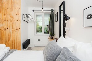A bedroom with a bed, a radiator, a window with curtains, a bedside table with a lamp, and a framed picture on the wall.