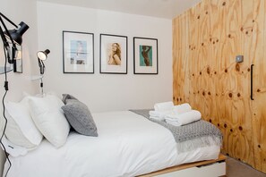 A bedroom with a bed, pillows, a blanket, a wooden wardrobe, and framed pictures on the wall.
