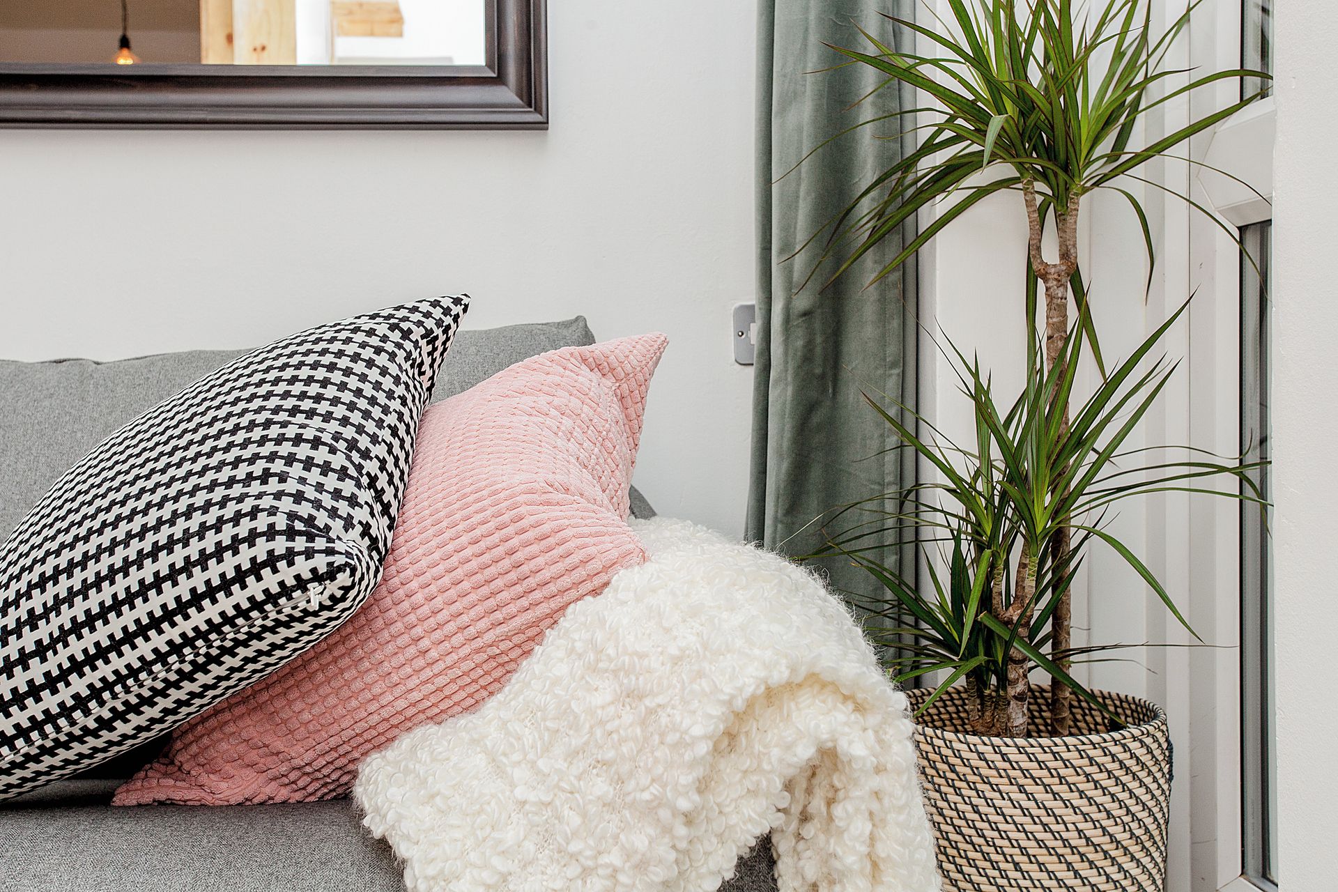 Un canapé agrémenté de coussins à motifs, une couverture blanche et moelleuse, et une plante en pot.